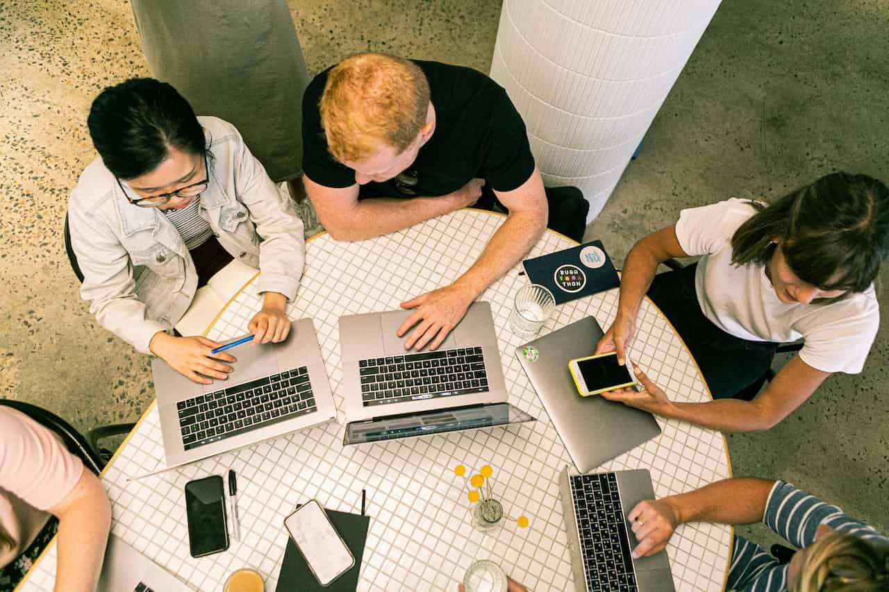 people sitting at a desk with laptops in front of them