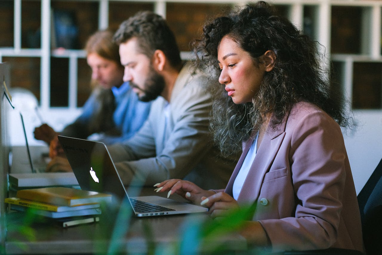 three people sitting at a desk in front of laptops