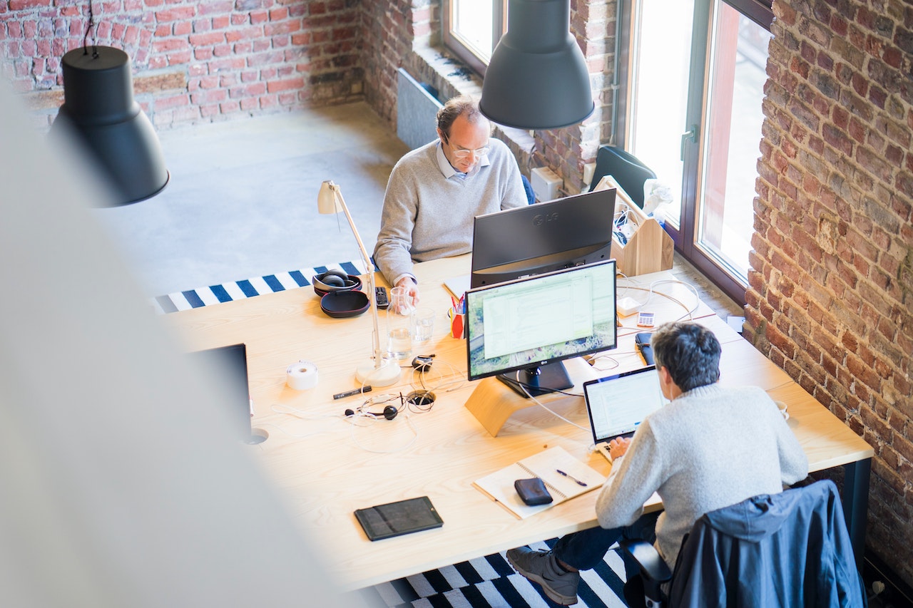 two men sitting in front of computers in an office space