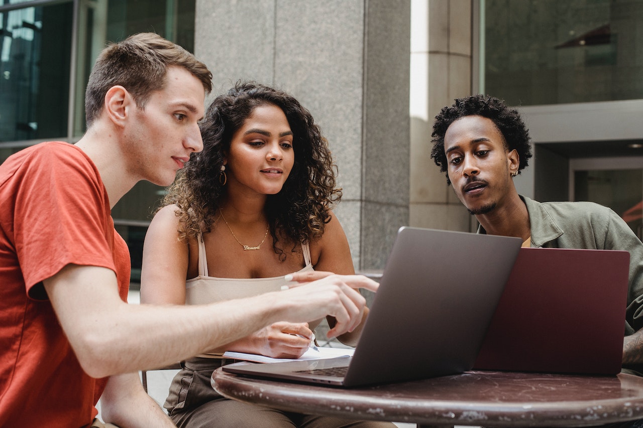 a group of people by a table, looking at a computer's screen