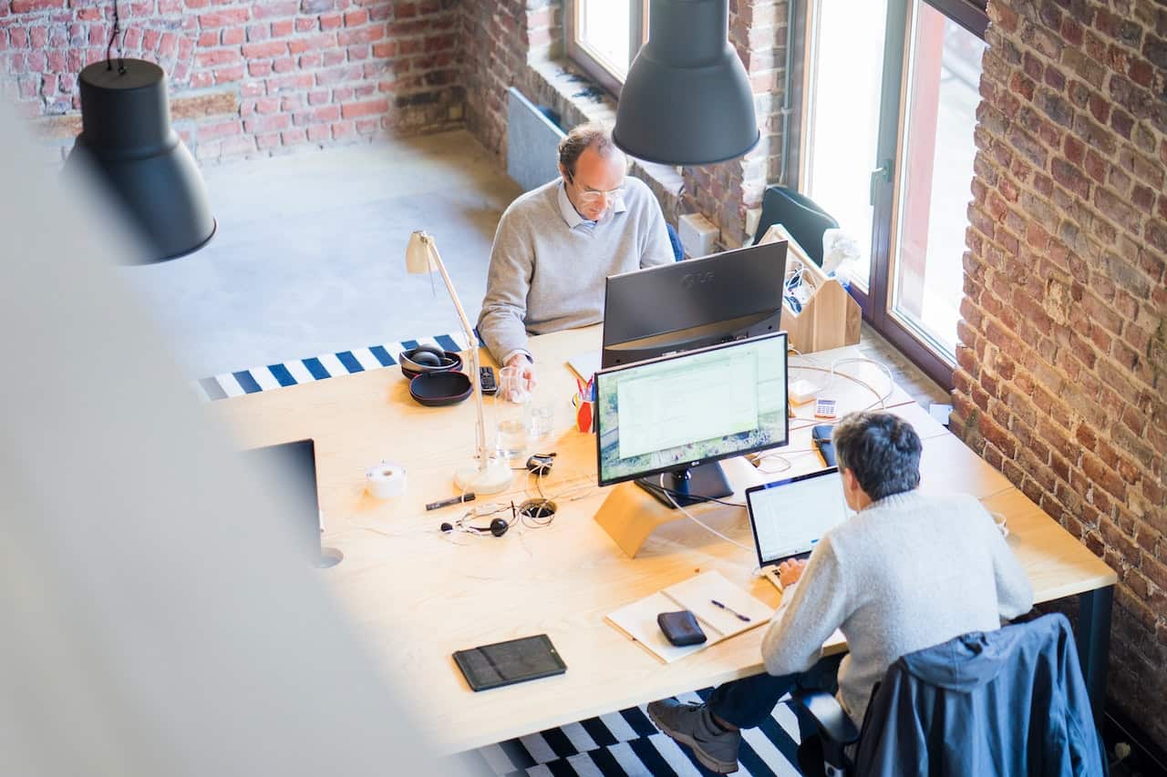 Two men sitting at a desk, working on laptops